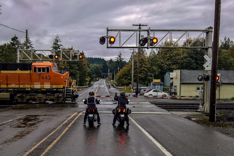 dwóch motocyklistów przed przejazdem kolejowym w deszczowy dzień