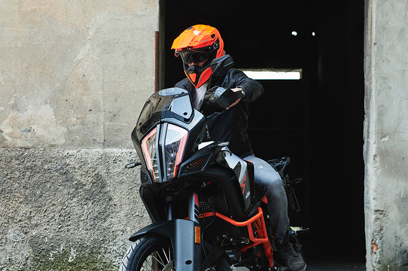 Motocyklista w pomarańczowym kasku na sportowym motocyklu wyjeżdżający z budynku