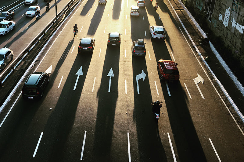 Sześciopasmowa autostrada z jadącymi autami i motocyklem, oznaczenia drogowe i padające słońce na ulicę