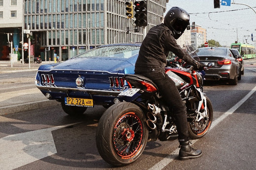 motocyklista na drodze obok niebieskiego samochodu w oczekiwaniu na zielone światło. 