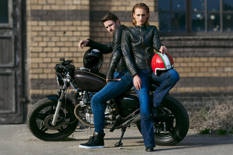 Para motocyklistów pozującą przy motocyklu w skórzanych kurtkach motocyklowych, obydwoje trzymają kaski i mają na sobie jeansy motocyklwoe