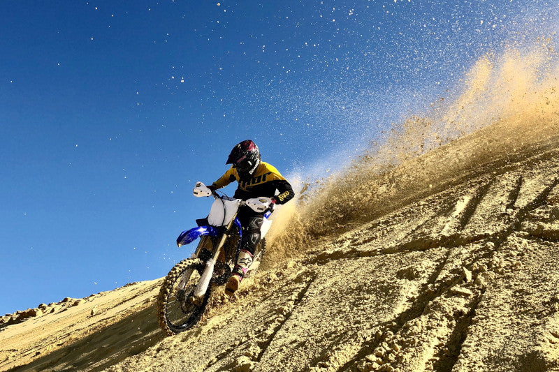 motocyklista jedzie w dół wzgórza rozsypując piach 