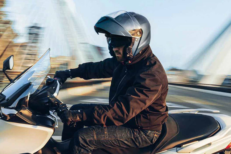 motocyklista na motocyklu w szarym kasku szczękowym oraz tekstylnej kurtce motocyklowej