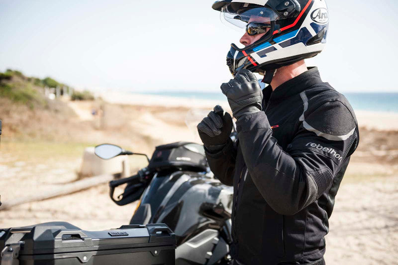 motocyklista stojący na skraju plaży zakłada kask typu adventure