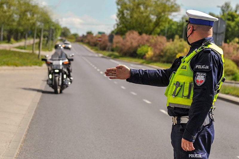 Policjant na drodze zatrzymujący motocyklistę, wskazujący mu dłonią miejsce zjechania na pobocze