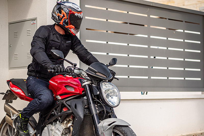 Motocyklista w malowanym kasku na sportowym motocyklu, wyjeżdżający z budynku, patrząc w lewo