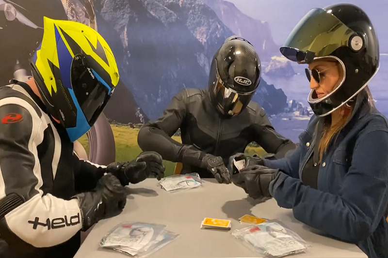 Trzech motocyklistów w ubranych kaskach, grających w karty, na stole maseczki