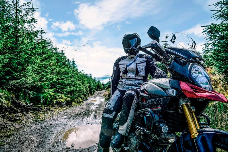 turysta motocyklowy siedzi na motocyklu typu adventure w środku lasu, jest ubrany w zestaw motocyklowy rst