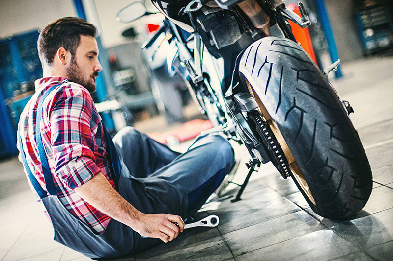 mechanik siedzi w warsztacie zmieniający olej silnikowy w motocyklu