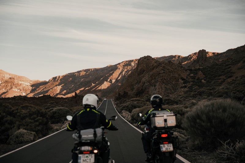 para motocyklistów w kurtkach Rebelhorn jedzie obok siebie drogą dwupasmową w kierunku zachodzącego słońca