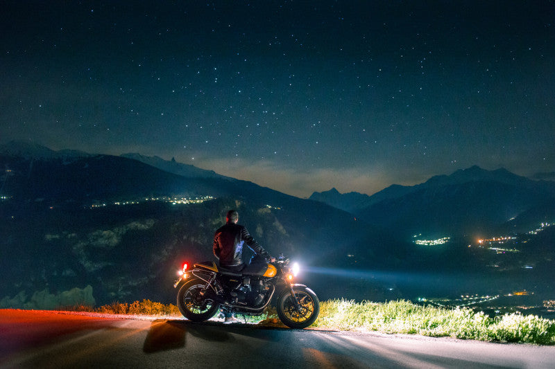 Motocykl z motocyklistą w nocy przy gwieździstym niebie z widokiem na góry