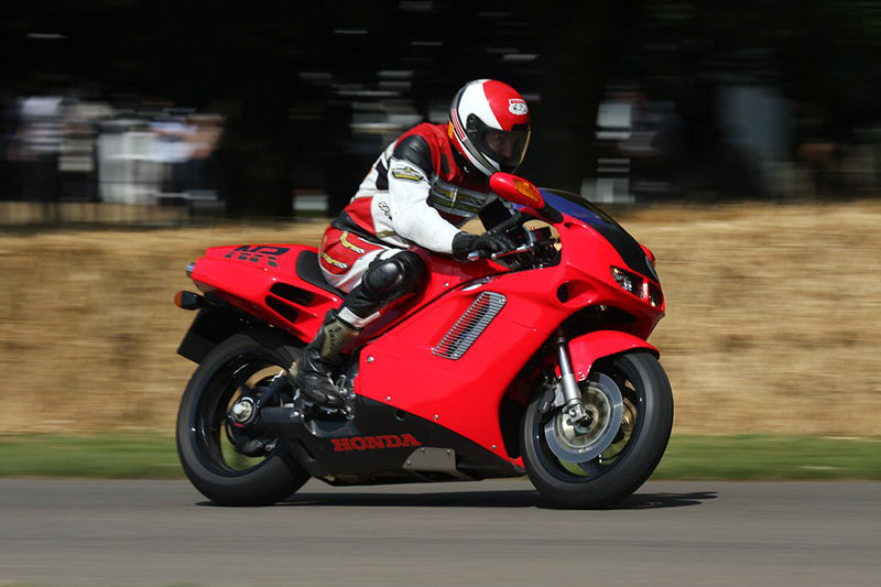 Sportowy motocykl kultowy na torze motocyklowym, kierowca w kasku i biało czerwonym kombinezonie