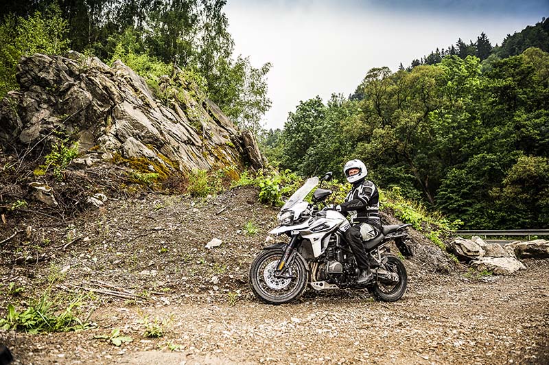 mężczyzna na swoim motocyklu turystycznyhm stoi w terenie przy skałkach