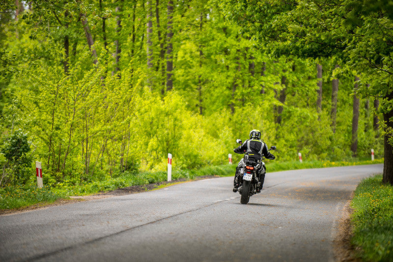 Motocyklista na pobocznej drodze w gęstym lesie, w kasku i kombinezonie motocyklowym 