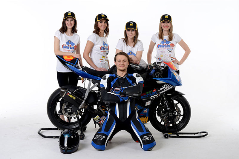 profesjonalny zawodnik Paweł Rinas Przybylski klęczy przy motocyklu, za nim stoją 4 kobiety