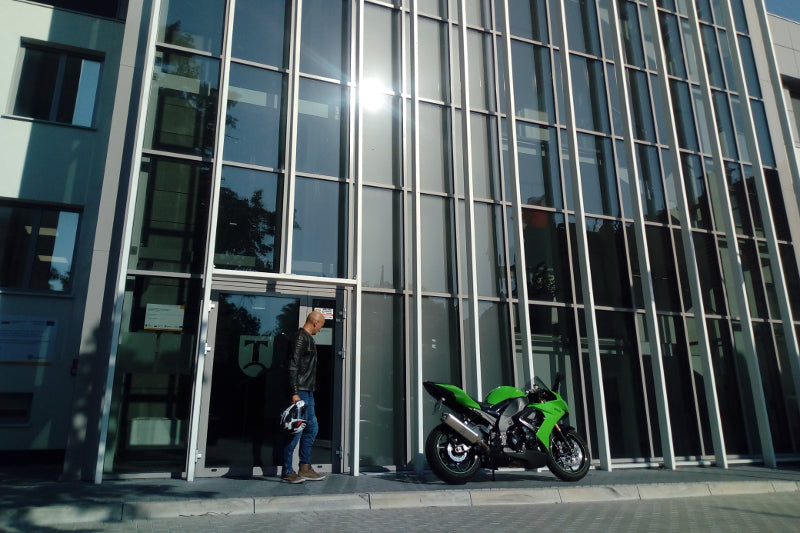 mężczyzna ubrany w klasyczny stój od Rebelhorna wychodzi z budynku, obok stoi zielony motocykl