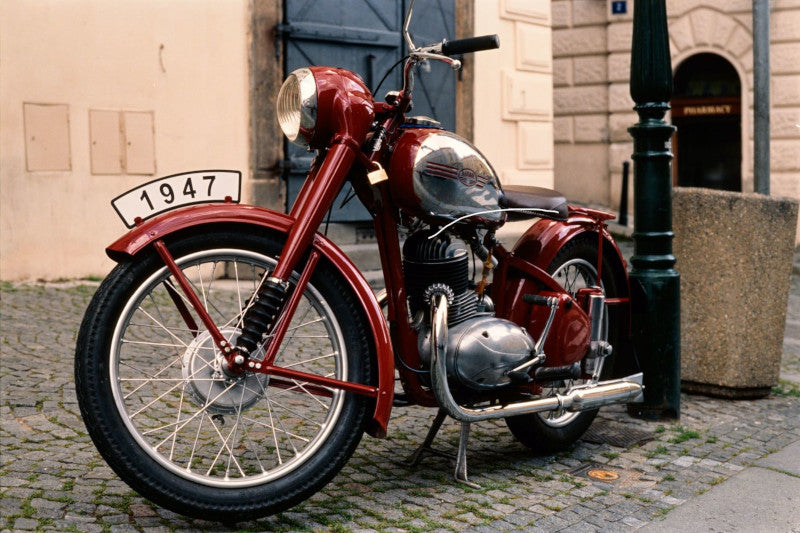 czerwony motocykl przy latarni miejskiej z tabliczką na przednim kole z napisem 1947