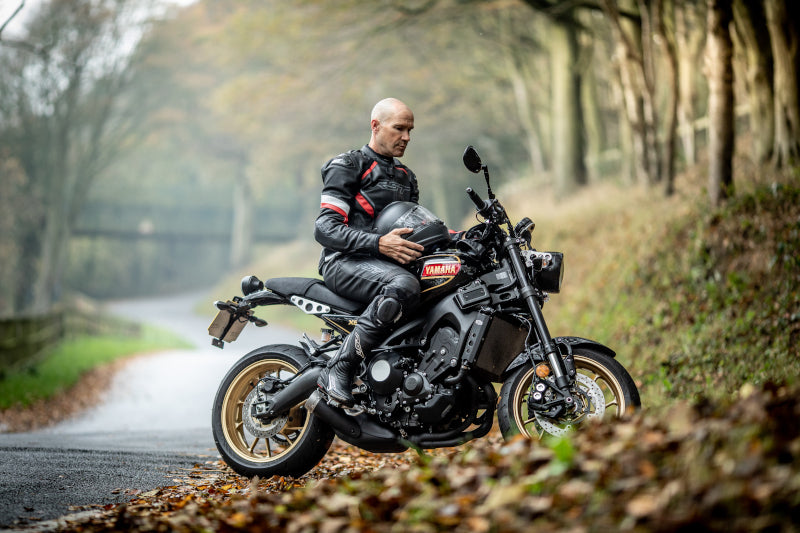 motocyklista na motocyklu jesienną porą na poboczu leśnej drogi wśród jesiennych liści. 