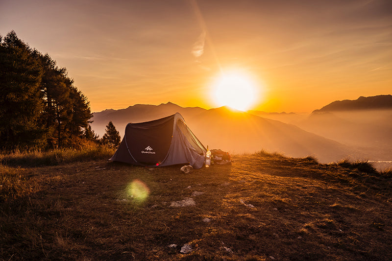 zachód słońca nad górami i namiotem zlokalizowanym na polanie 
