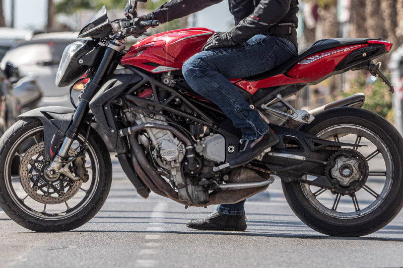 motocyklista siedzi na czerwonym motocyklu w kompletnym stroju motocyklowym, zbliżenie na tanie buty motocylowe