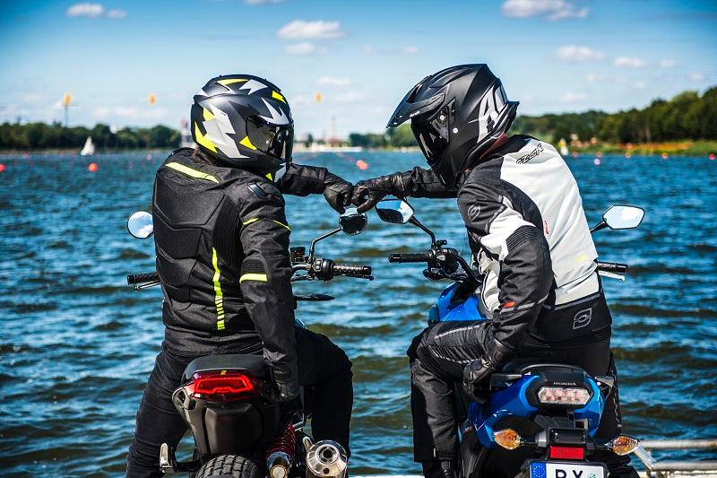 dwoje motocyklistów zaparkowało nad morzem i przybijają żółwika tanimi rękawicami motocyklowymi