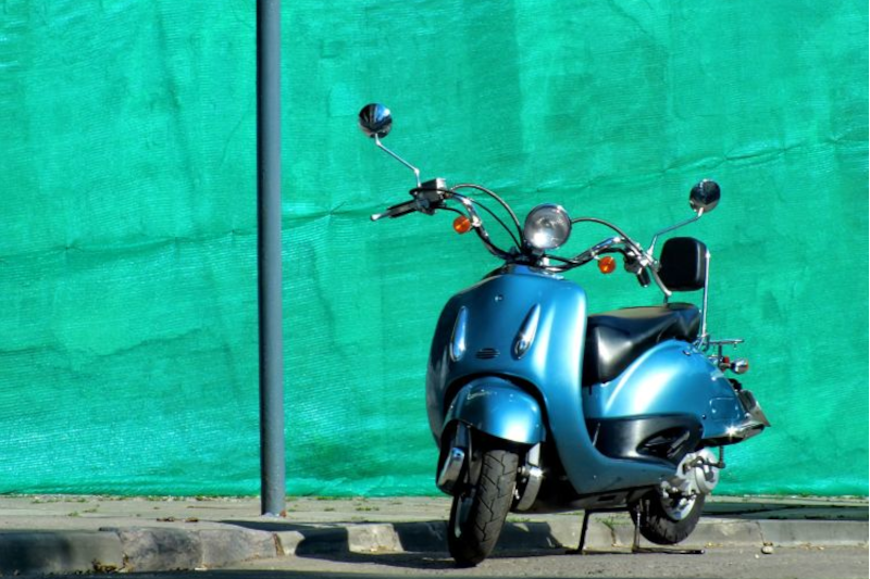 Niebieski skuter w stylu retro zaparkowany na ulicy, w tle zielona ściana