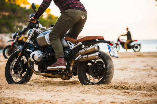 zdjęcie tłumika motocyklowego, motocykl stoi na piachu, jedzie na nim motocyklista ubrany w zielone spodnie i czerwoną koszulę