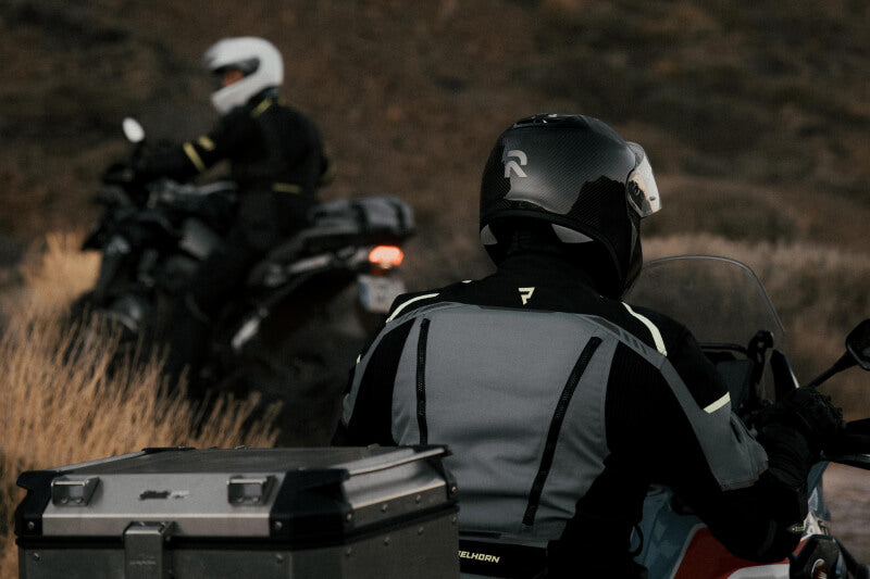 Motocyklista w kasku motocyklowym i turystycznej kurtce, poprawiający rękawice motocyklowe, stojący przy motocyklu turystycznym