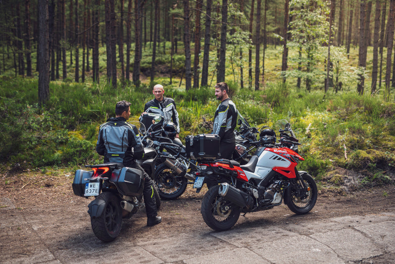 trójka motocyklistów stoi podczas przerwy w wyprawie w lesie